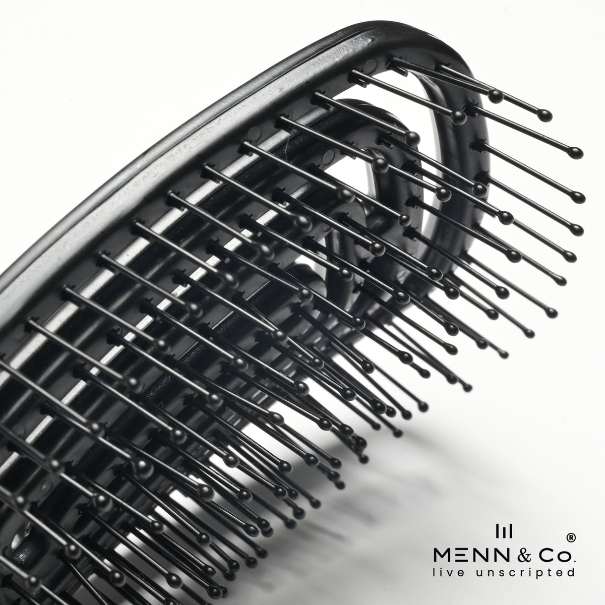 Close-up of a black hairbrush with flexible bristles, shown on a clean white background with the MENN & Co logo in the bottom right corner.