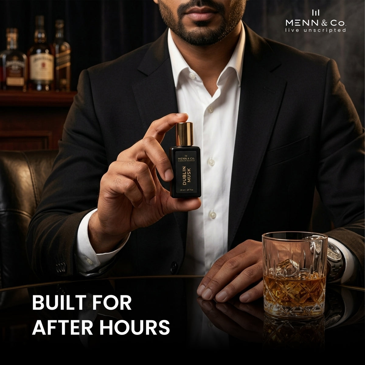 Man holding a bottle of Menn & Co. perfume with a glass of whiskey on a dark background