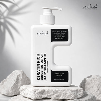 A white pump bottle of Menn & Co Keratin Rich Color Protection Hair Shampoo, styled on white stones against a light gray background with soft leaf shadows.