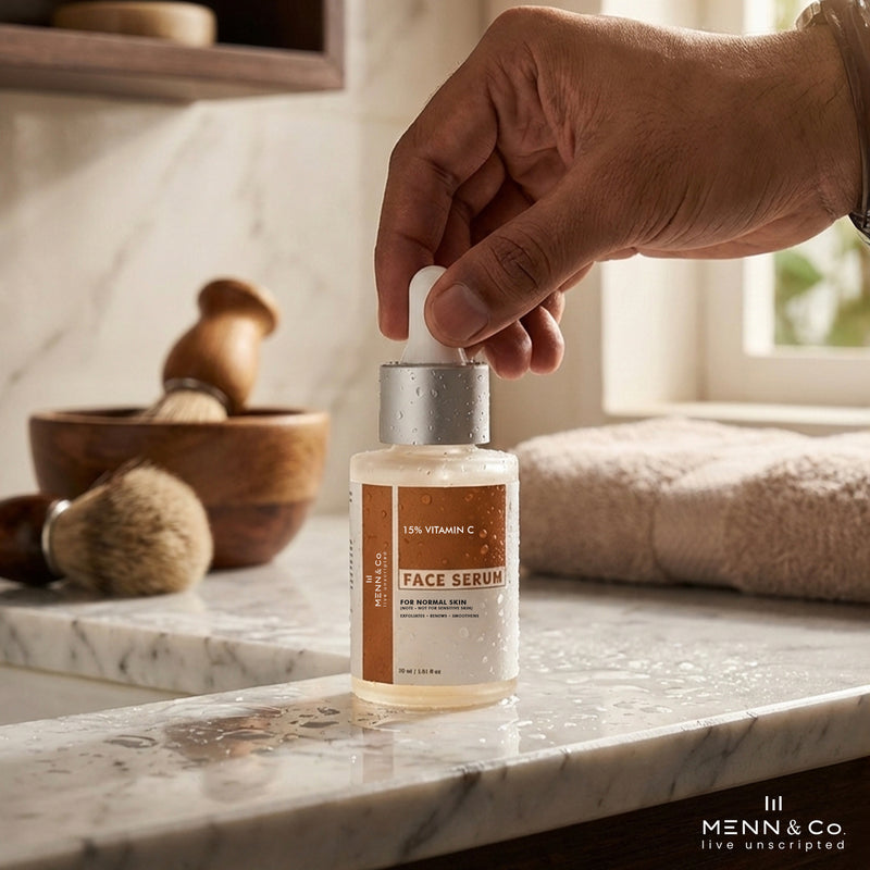Hand holding a bottle of Menn & Co Vitamin C face serum on a marble counter with grooming items in the background