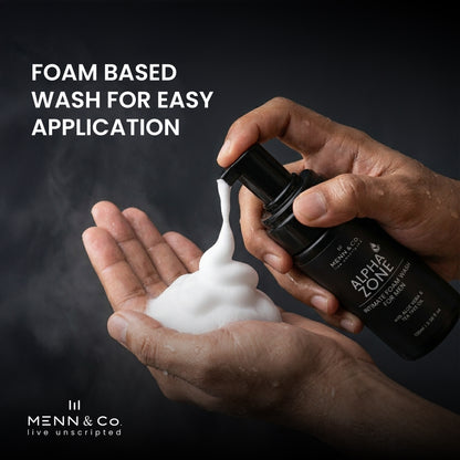 Hand holding a bottle of Menn & Co Alpha Zone wash with foam being dispensed onto another hand against a dark background.