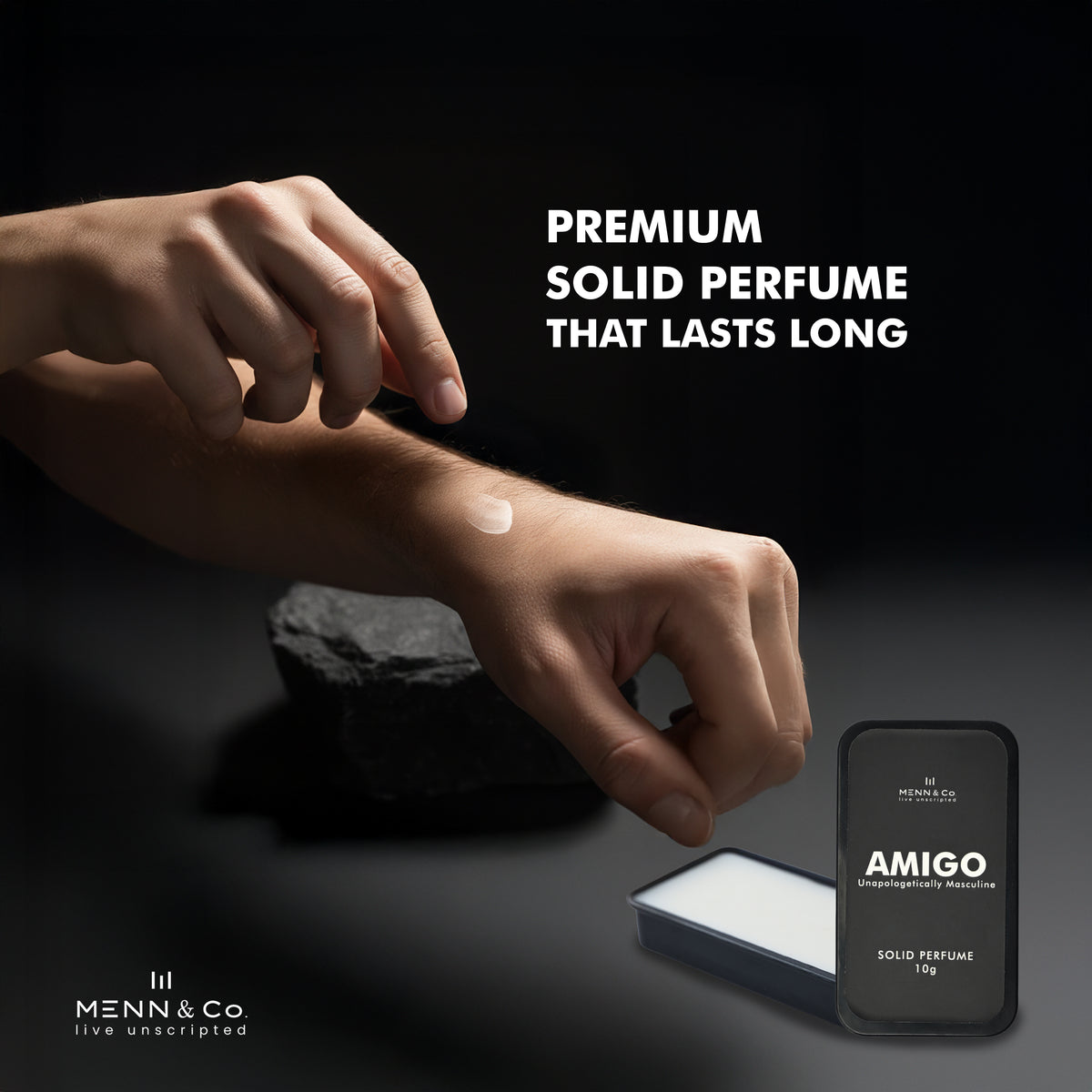 Hand applying solid perfume to wrist with 'AMIGO' solid perfume packaging on a dark background