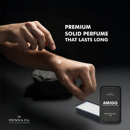 Hand applying solid perfume to wrist with 'AMIGO' solid perfume packaging on a dark background