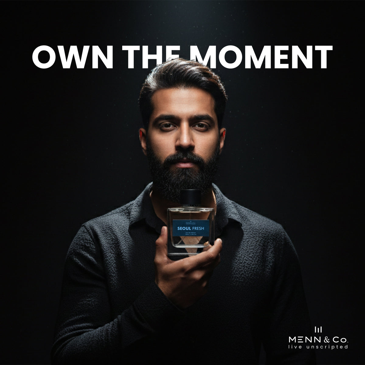 Man holding a bottle of 'Seoul Fresh' cologne with 'Menn & Co' branding and 'Own The Moment' text on a dark background.