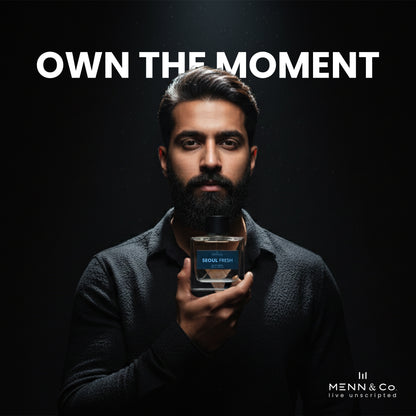 Man holding a bottle of 'Seoul Fresh' cologne with 'Menn & Co' branding and 'Own The Moment' text on a dark background.