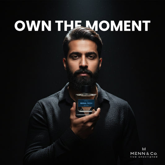Man holding a bottle of 'Seoul Fresh' cologne with 'Menn & Co' branding and 'Own The Moment' text on a dark background.