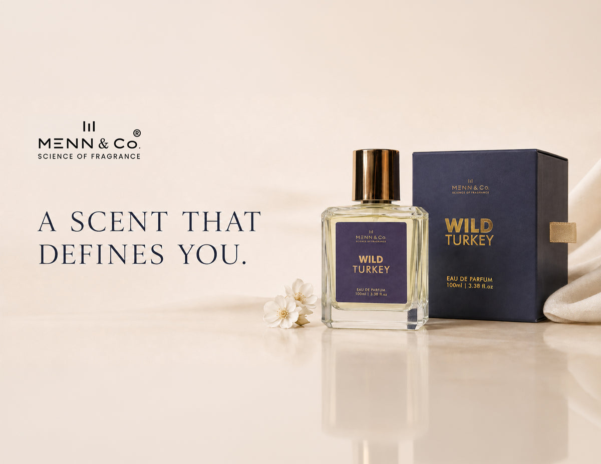 Menn & Co Wild Turkey Eau de Parfum bottle with a gold cap next to its navy blue box, set on a reflective beige surface with a small white flower and draped white fabric.