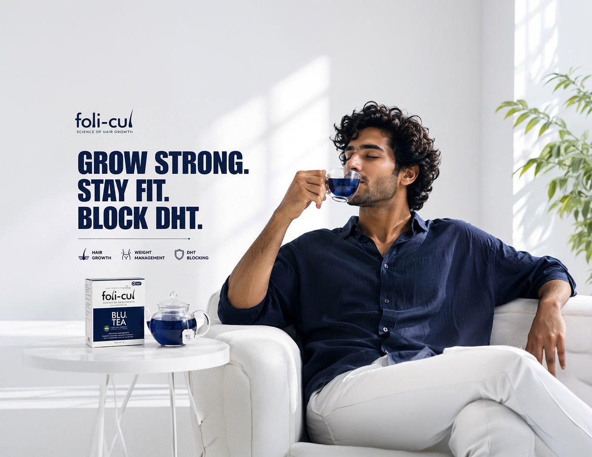 A man in a navy blue shirt and white pants relaxes on a white sofa, drinking from a blue cup. A foli-cul tea box and matching blue cup sit on a small white side table beside him in a bright, modern room with natural light.