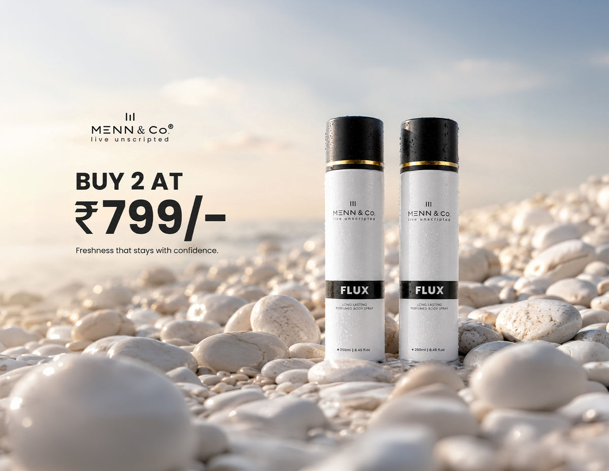 Two white and black Menn & Co Flux haircare bottles standing on white pebbles with a beach background and promotional text on the left.