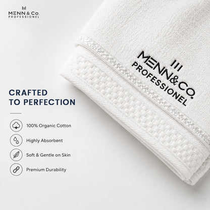 A folded white cotton towel with black printed Menn & Co Professional branding, shown on a clean white background with marketing text highlighting organic cotton, absorbency, softness, and durability.