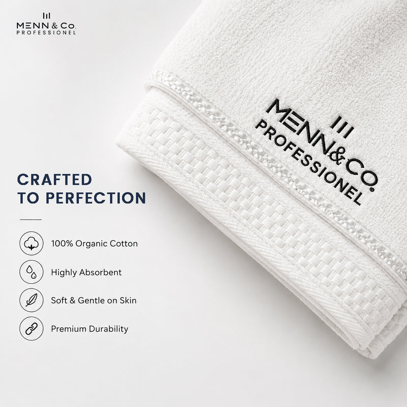 A folded white cotton towel with black printed Menn & Co Professional branding, shown on a clean white background with marketing text highlighting organic cotton, absorbency, softness, and durability.