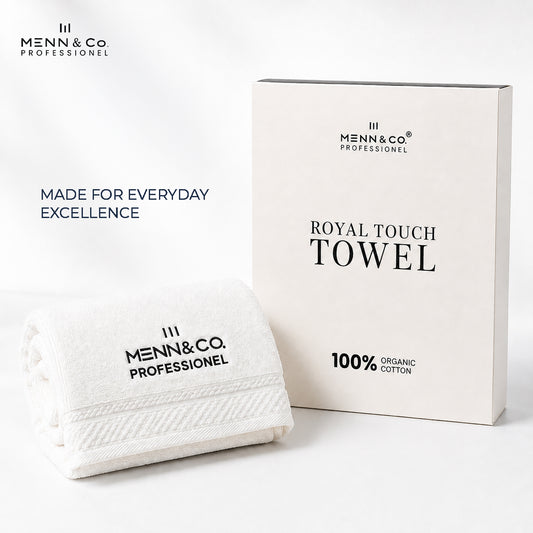 A folded white cotton towel with black printed branding sits in front of its matching off-white product box. The packaging reads 'ROYAL TOUCH TOWEL' and '100% ORGANIC COTTON,' and the towel reads 'MENN&Co PROFESSIONEL.