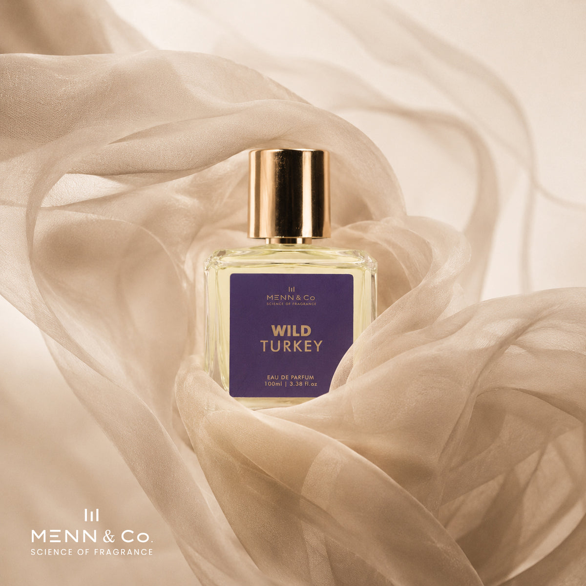 A bottle of Menn & Co Wild Turkey Eau de Parfum centered on draped beige fabric. The bottle is clear glass with pale yellow liquid inside, a metallic gold cap, and a dark purple label with gold lettering.